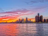 Detroit Skyline at sunset, with the river in the foreground and a purple-orange hued sky
