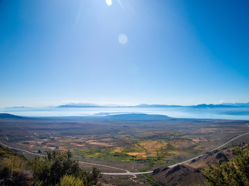 Wide aerial view of Mono Lake in the fog against the blue sky, and road weaving across the landscape