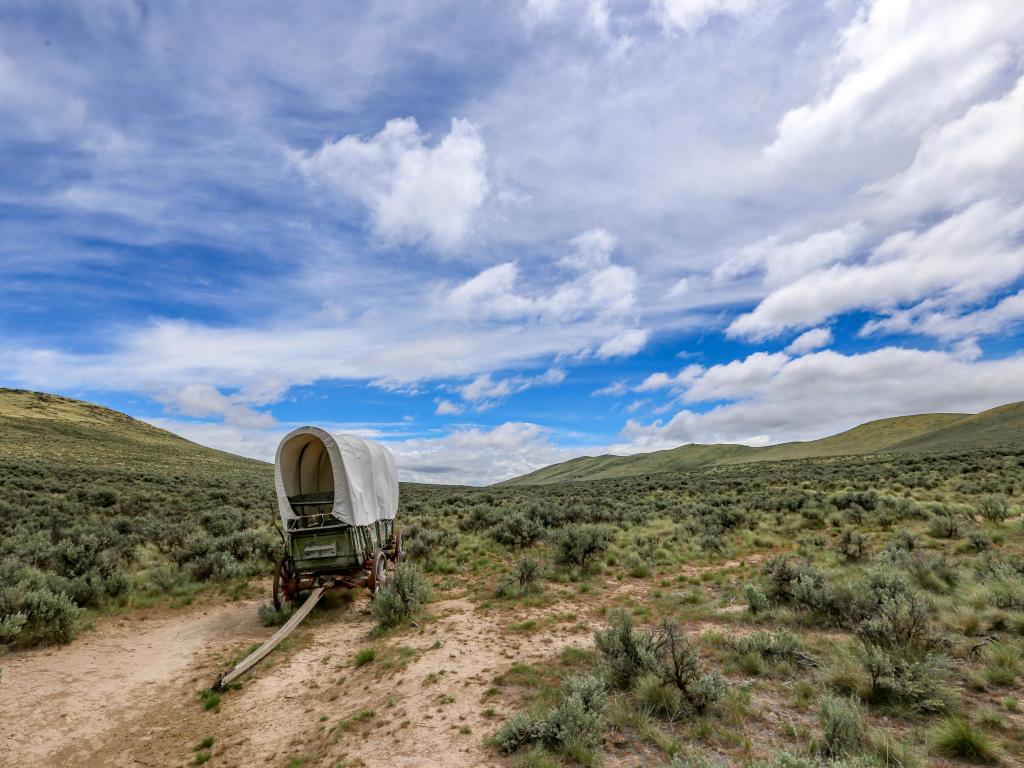 A historic wagon stands on a path in the mountains on the Oregon Trail near Baker City, with a blue sky above