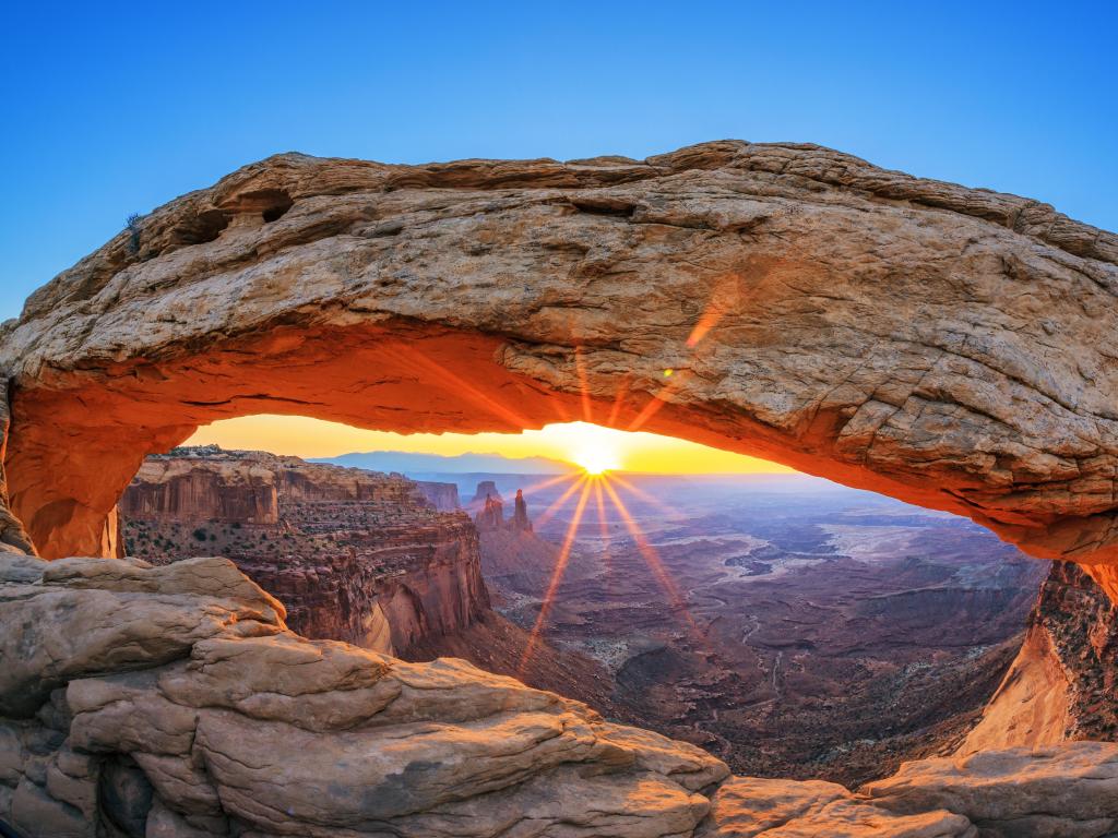 Canyonlands National Park near Moab, Utah, USA taken at sunrise with the sun through the Mesa Arch against a blue sky and the valleys beyond in the distance. 