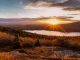 Gentle hill slopes covered in forest in the foreground, with sun setting over the water behind