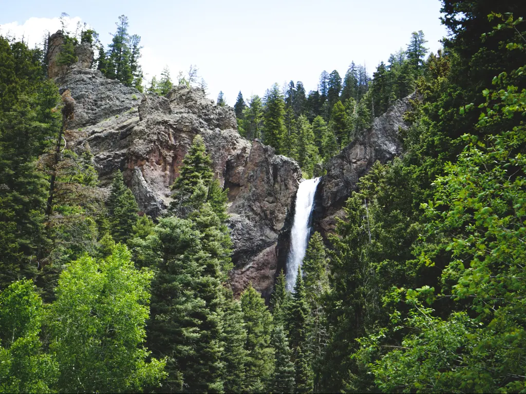 Shot from below of the cascading waters of Treasure Falls in the Rocky Mountains, Colorado, with lush green trees in the foreground