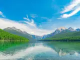 Glacier National Park, Montana, USA with a closeup of the Bowman Lake with trees and mountains in the distance against a blue sky.