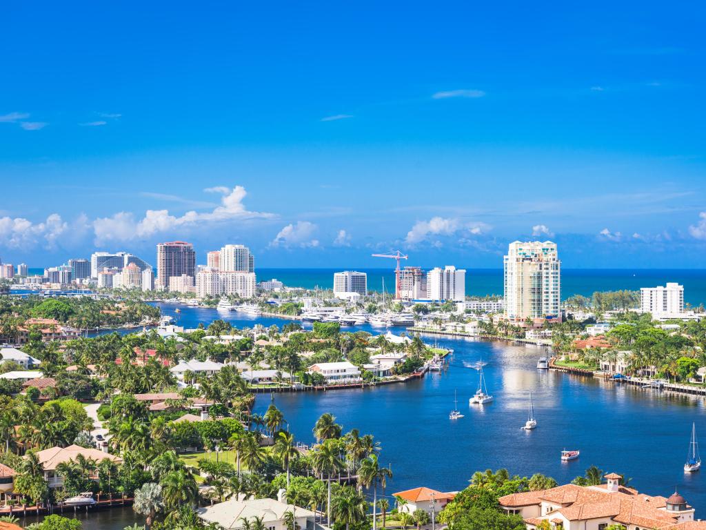 Fort Lauderdale, Florida with yachts in the water, trees and buildings in the foreground and the tall city buildings in the background with the sea beyond. 