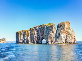 Perce Rock, Gaspe Peninsula, Quebec, Canada with the sea in the foreground and the cliff formation in the background on a clear sunny day.