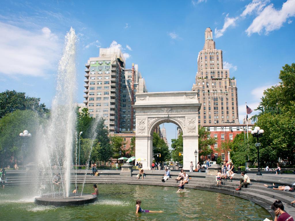 View of arch and fountains surrounded by buildings and clear, blue, sky at Washington Square Park