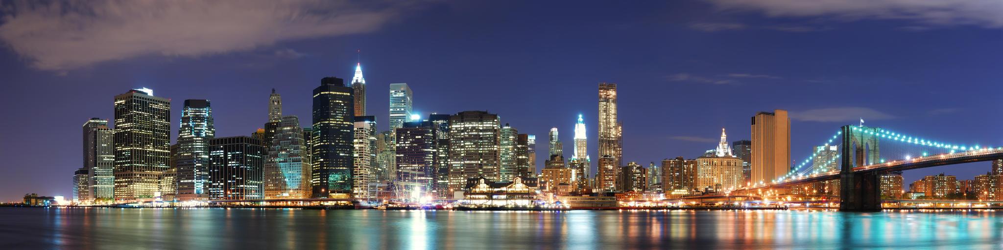 View of high rise buildings and illuminated Brooklyn Bridge at night, from across the river