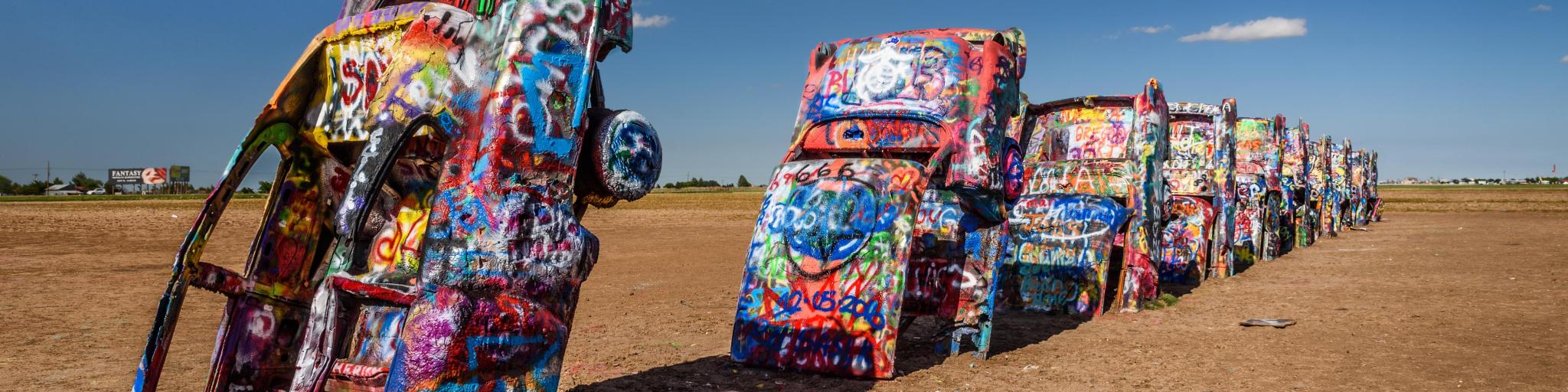 Cadillac Ranch in Amarillo, a popular landmark on historic Route 66, on a sunny day. There are several Cadillac cars in the sand, upside down.