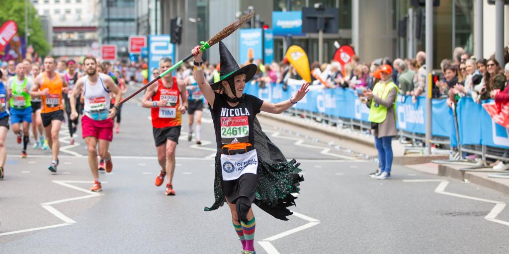 Happy Marathon runner dressed as a witch being cheered by the public