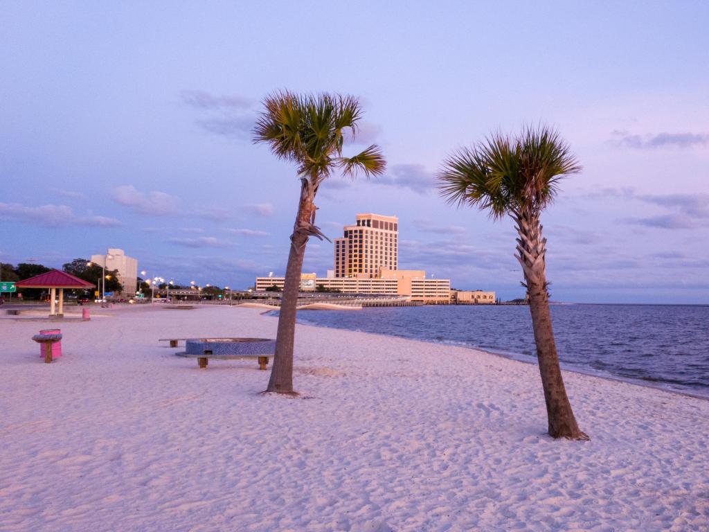 Biloxi, Mississippi Gulf Coast, USA with palm trees in the sand, the sea and buildings in the distance taken at early evening.