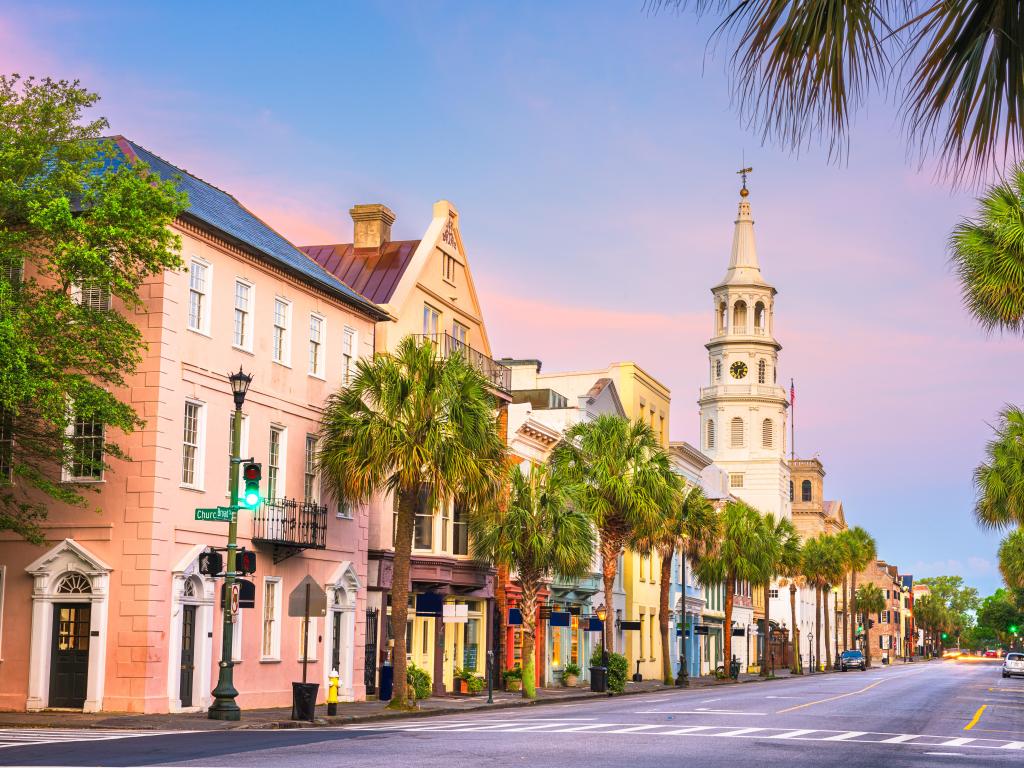 Charleston, South Carolina, USA taken at the French Quarter at twilight with beautifully painted buildings and a church in the distance, palm trees lining the street.