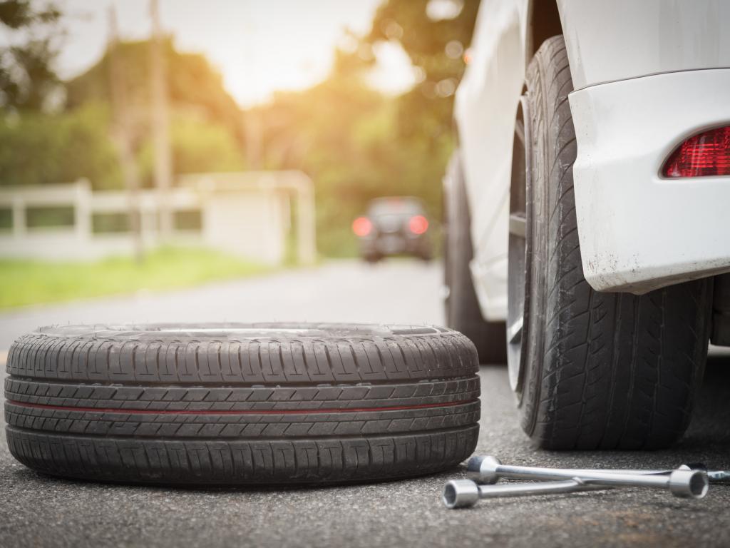 Spare tire about to go onto a car to replace a puncture with a donut.