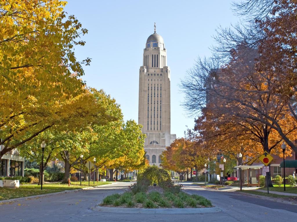 The Nebraska State Capitol Building in downtown Lincoln with trees in fall colors lining the road