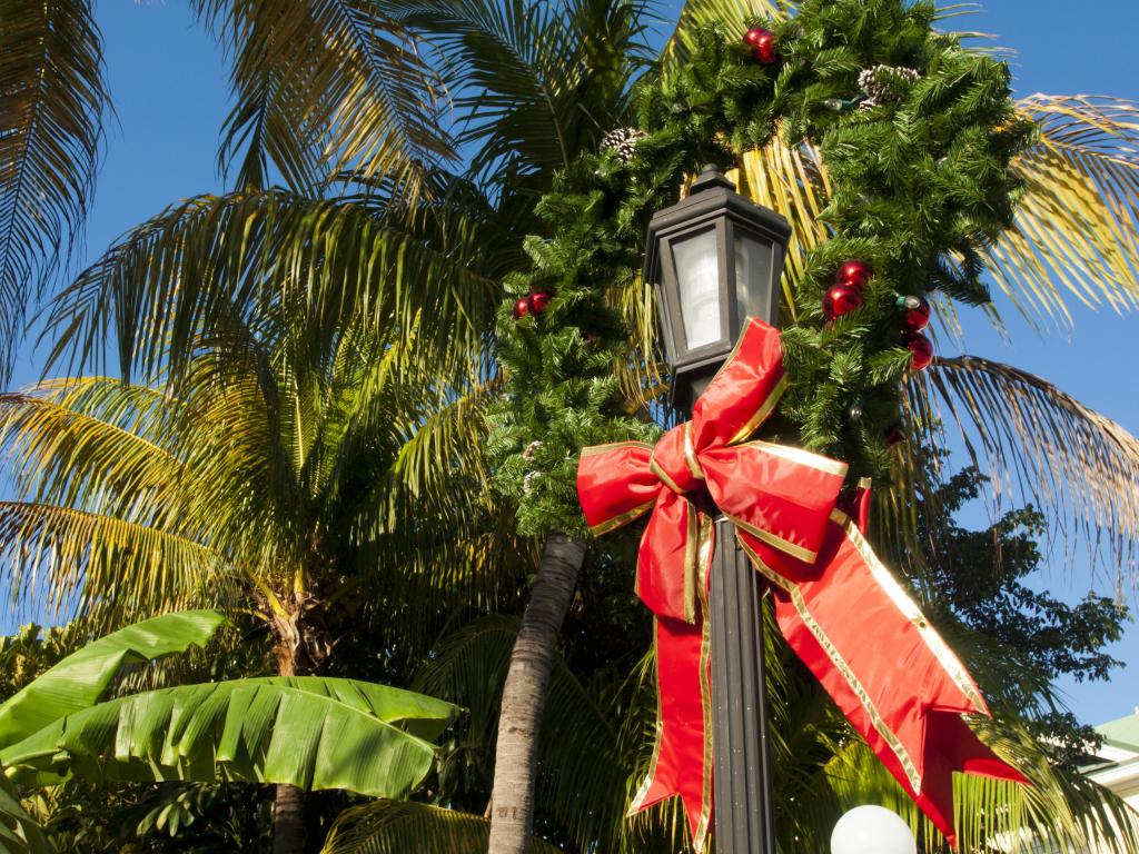 Palm trees and a light post, wrapped in a Christmas ribbon with a wreath, with blue skies in the background