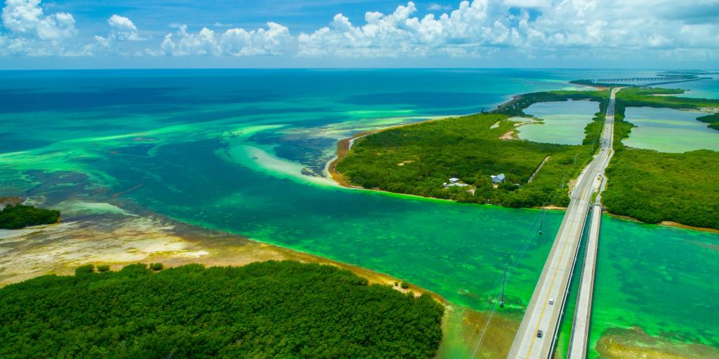 An aerial view overseas highway surrounded by green and blue waters and sandy islands as it comes into to Key West, Florida Keys, USA. 