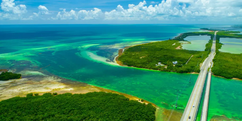 An aerial view overseas highway surrounded by green and blue waters and sandy islands as it comes into to Key West, Florida Keys, USA. 