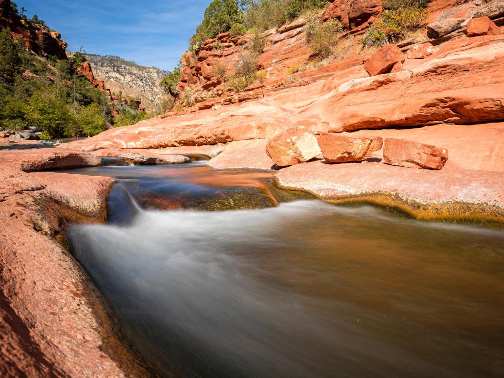 Slide Rock State Park, Arizona, USA with a rock water slide in the foreground and the Oak Creek Canyon in the background.