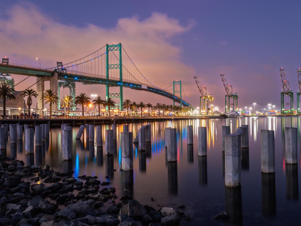 Long Beach, CA, USA with the Vincent Thomas Bridge connecting Long Beach and San Pedro taken at night with trees lining the waters edge. 