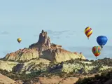 A group of hot air balloons rise above the red sandstone of Red Rocks State Park near Gallup, New Mexico, and circle around the Church Rock formation