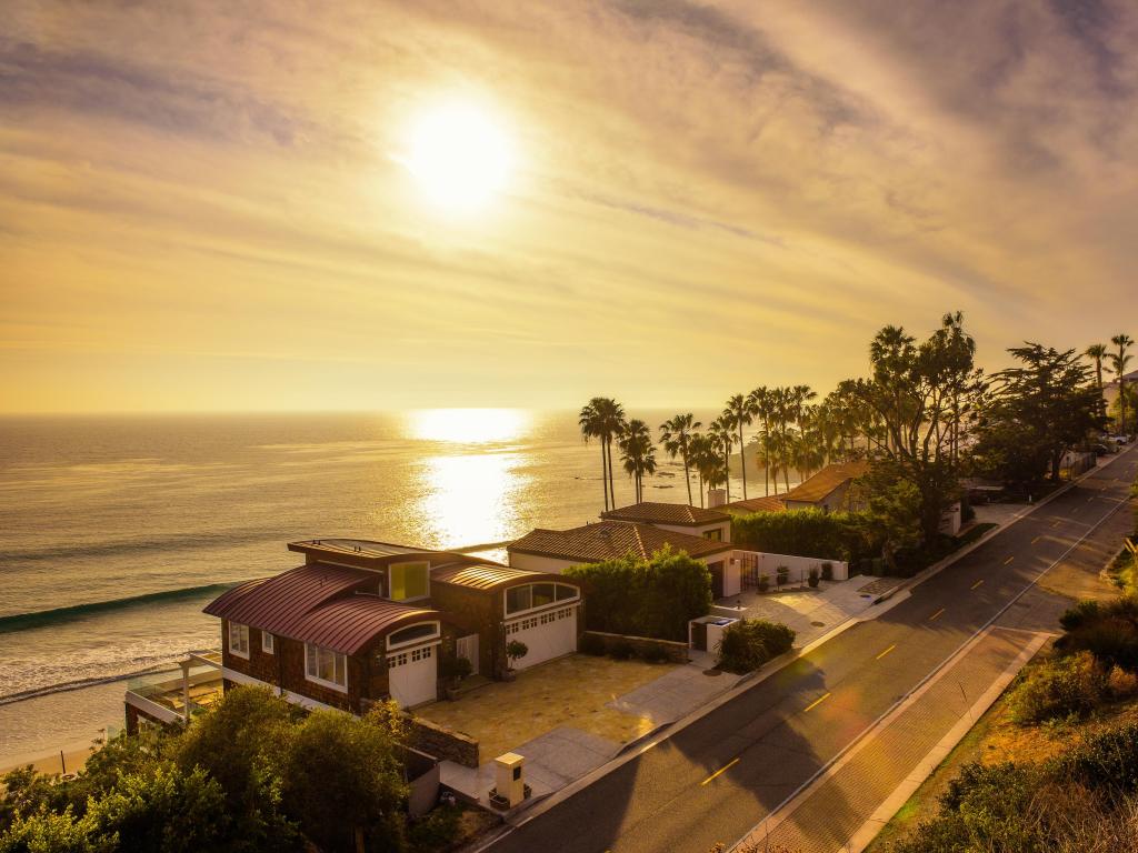 Malibu beach, near Los Angeles, California with luxury oceanfront homes overlooking the beach at sunset, trees in the distance.