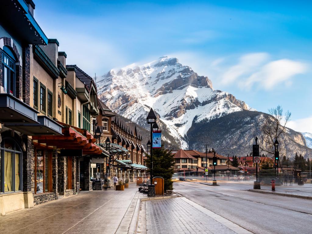 Banff, Canada with a view of a busy street at winter with the mountain in the distance covered in snow on a sunny day.