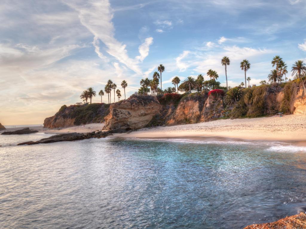 Laguna Beach, California, USA with a sunset view of Treasure Island Beach with cliffs and a cove below, trees in the distance.