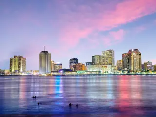 New Orleans, Louisiana with the downtown city in the background and the Mississippi River in the foreground at twilight under a pink sky.