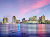 New Orleans, Louisiana with the downtown city in the background and the Mississippi River in the foreground at twilight under a pink sky.