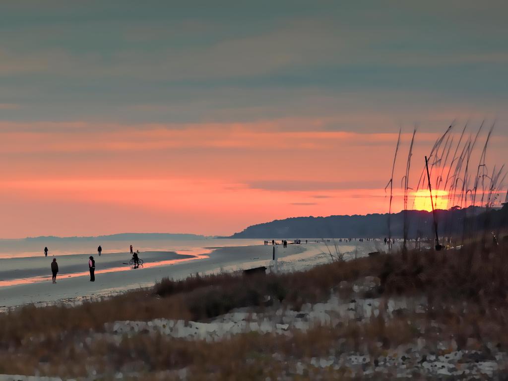 People walk on South Forest Beach on Hilton Head Island, with an orange sunset above