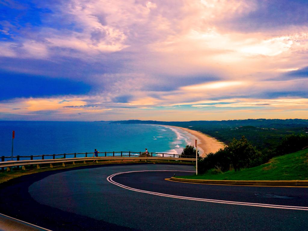 Road curves down towards sandy beach of Byron Bay at sunset