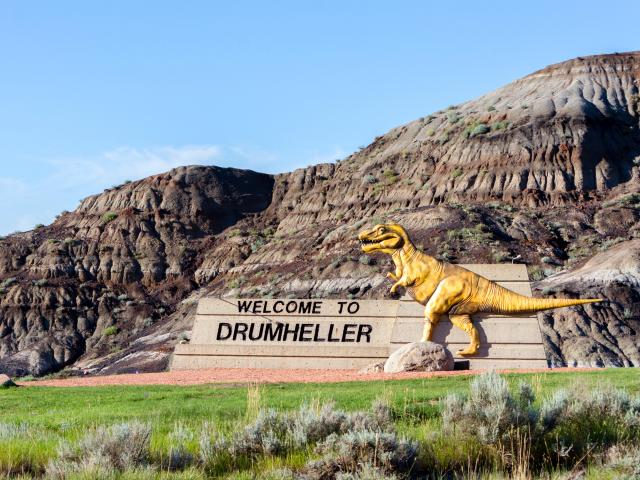 "Welcome to Drumheller" sign with dinosaur at the entrance to town on a sunny day