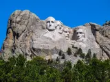 A scenic view of the 60-ft high granite sculpture of the four presidents of the United States in the Black Hills with a green forest at the foot of the mountain in a sunny morning in Mount Rushmore National Memorial Monument in South Dakota