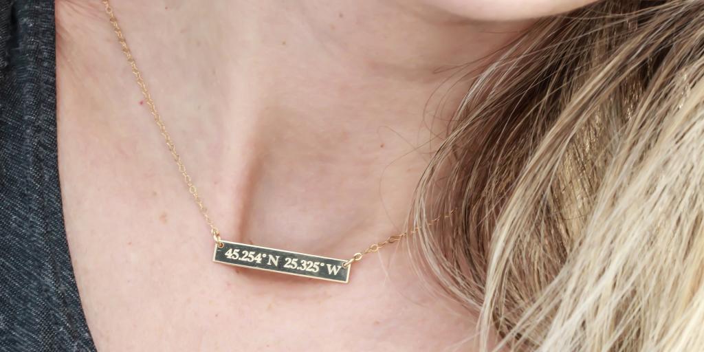 A close up of a woman wearing a gold necklace engraved with coordinates