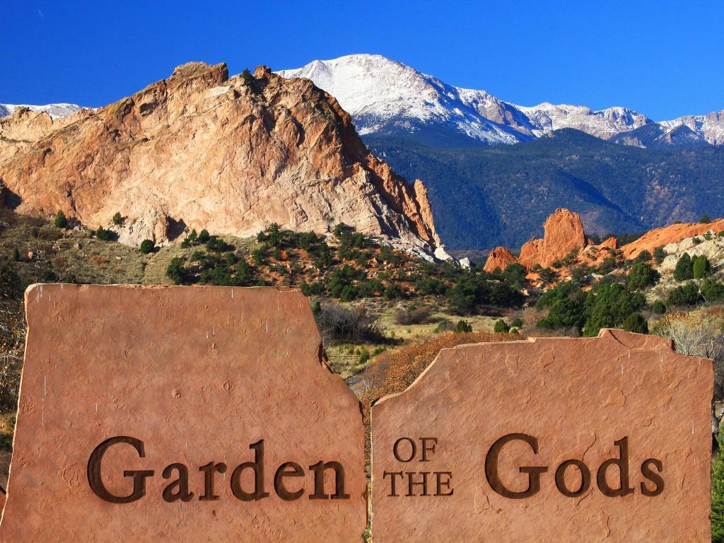 Red rock formations and Pikes Peak in the background from the park's East Entrance with the park's sign