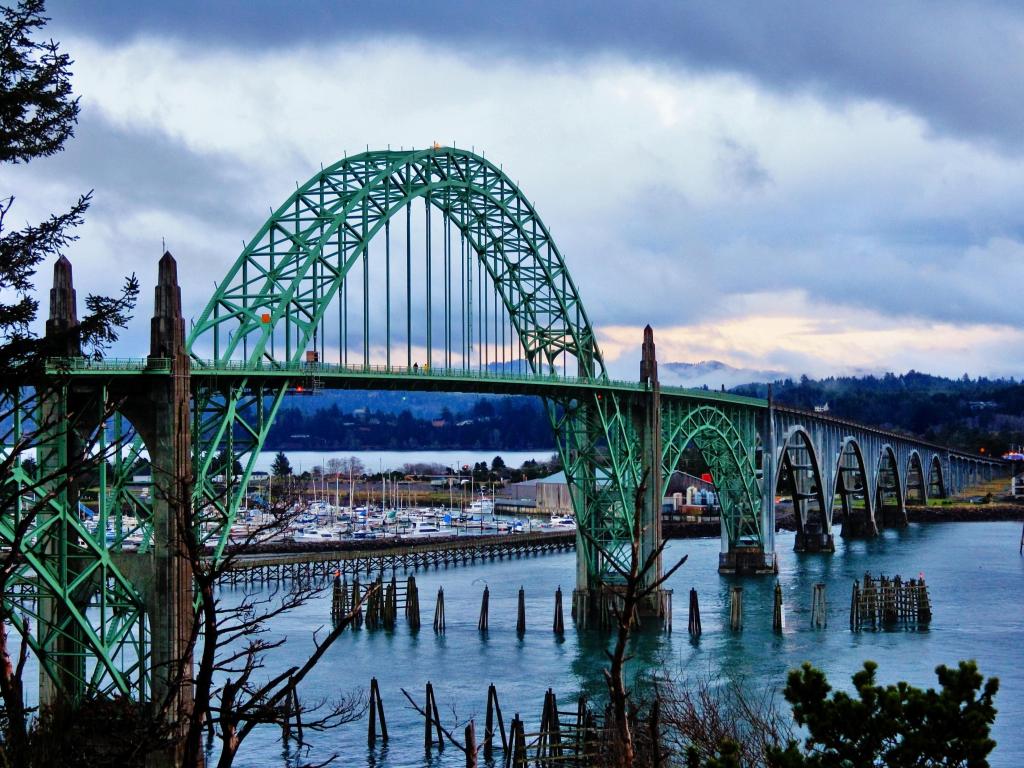 Green metal bridge crosses wide river with snow on the banks and atmospheric cloud