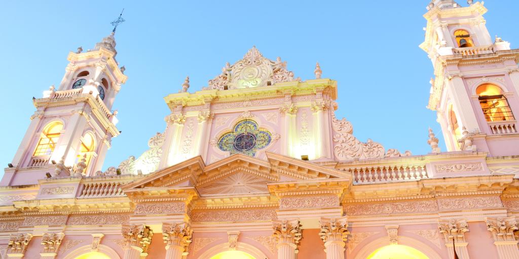 A close up of the baby pink exterior of Salta Cathedral with lights in the arches