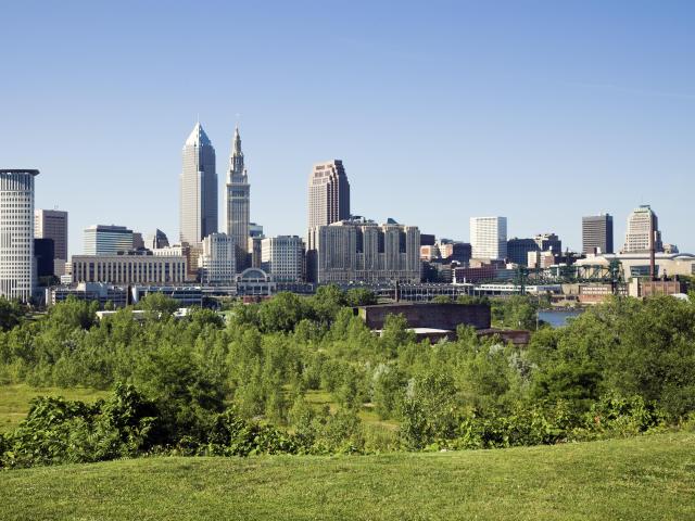Panoramic shot of downtown Cleveland, Ohio skyline on a summer's day, with green foliage in the foreground