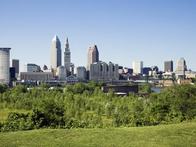 Panoramic shot of downtown Cleveland, Ohio skyline on a summer's day, with green foliage in the foreground