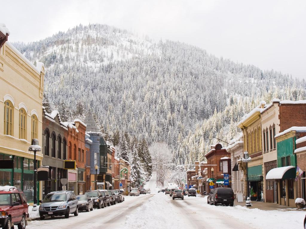 Wallace, Idaho, USA taken during winter of the downtown with snow and mountain in the background and rows of shops in the foreground.