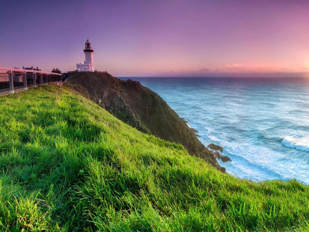Lighthouse on a cliff overlooking calm sea illuminated by pink sunrise light