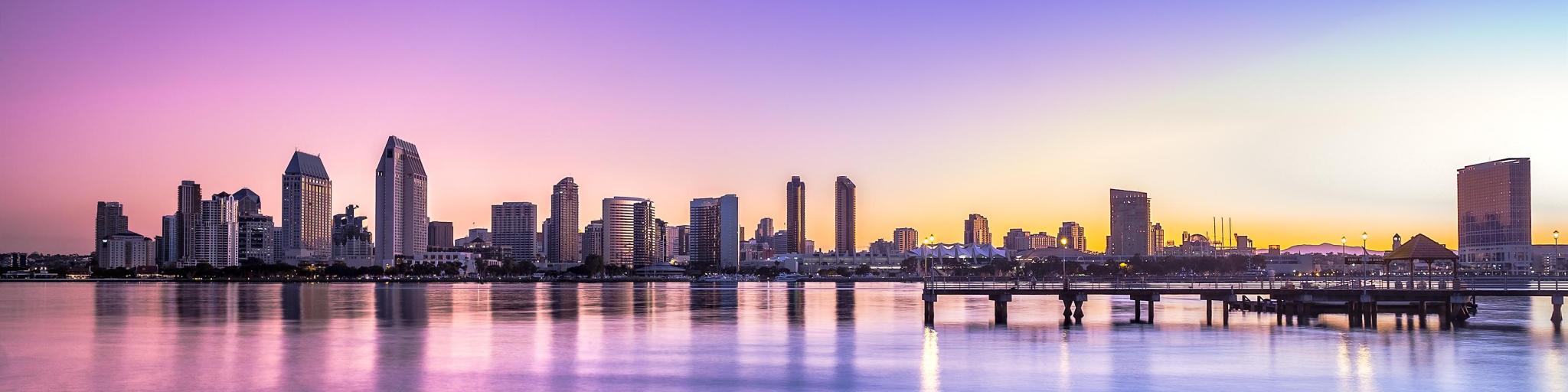 San Diego skyline at sunset with a pink and purple sky behind skyscrapers and water in front