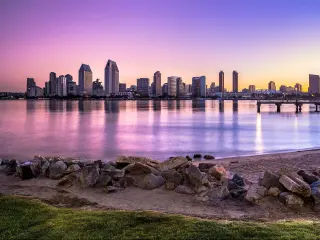 San Diego skyline at sunset with a pink and purple sky behind skyscrapers and water in front