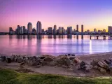 San Diego skyline at sunset with a pink and purple sky behind skyscrapers and water in front