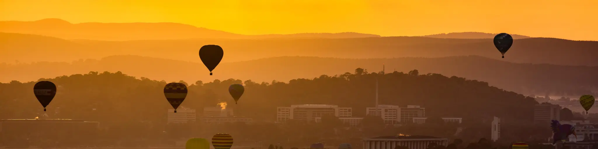 Hot air balloons are flying up during sunrise over the Lake Burley Griffin