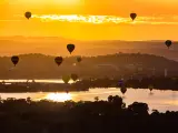 Hot air balloons are flying up during sunrise over the Lake Burley Griffin