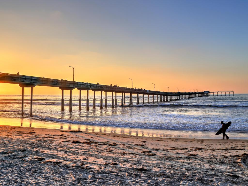 A surfer walks on Ocean Beach near the pier in San Diego, California.