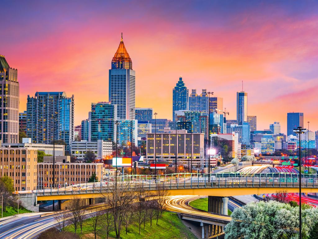 Busy downtown Atlanta at sunset, with a purple and orange-hued sky and streaming tail lights from traffic