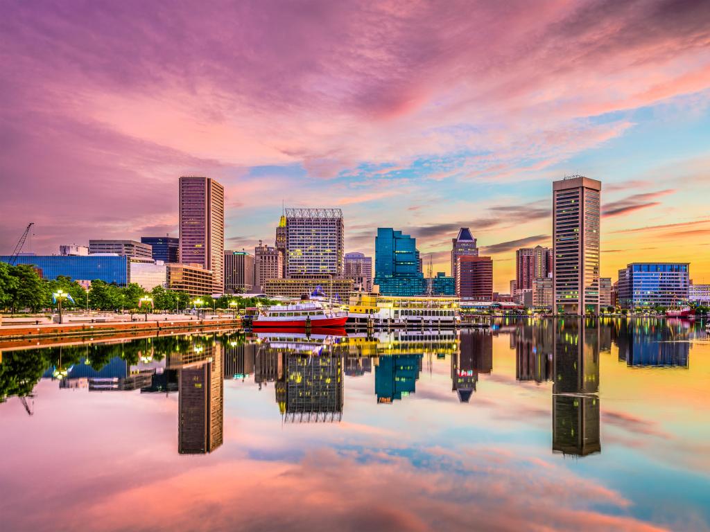 Baltimore, Maryland, USA with the city skyline on the Inner Harbor in the background and reflecting in the water in the foreground, taken at sunset with red and yellows in the sky.