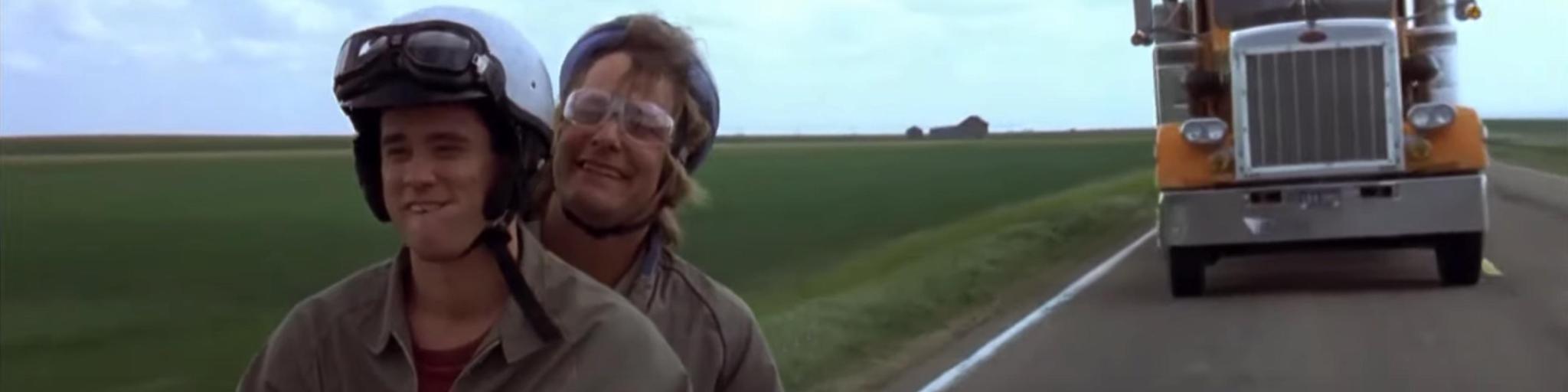 Still image from the Dumb and Dumber movie, showing the duo riding the famous bike with a truck approaching behind them
