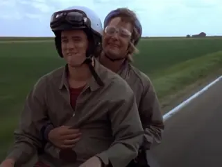 Still image from the Dumb and Dumber movie, showing the duo riding the famous bike with a truck approaching behind them